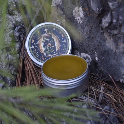Crema natural para dolor abierta con tapa al lado, agujas de pino difuminadas en primer plano